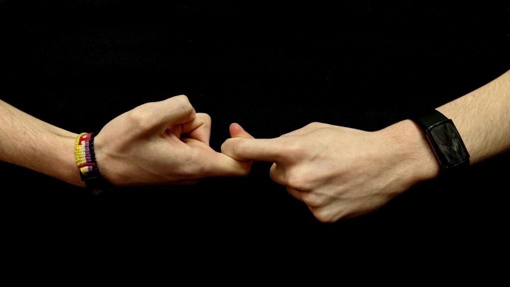 The hands of a young white person against a black background form the first half of the sign for “friendship” in American Sign Language.
